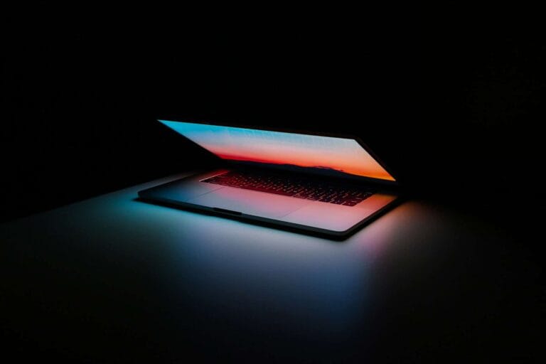 A partially closed laptop emits colorful light from its screen, with OLED burn-in risks in a dimly lit room.