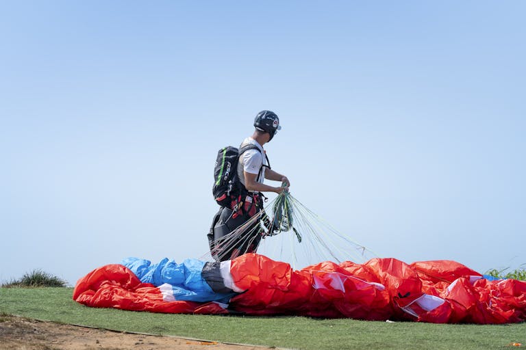 A person with gear prepares their parachute for paragliding on a clear day.