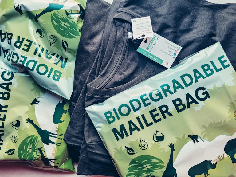 Close-up of biodegradable mailer bags and sustainable shirt promoting eco-friendly packaging.