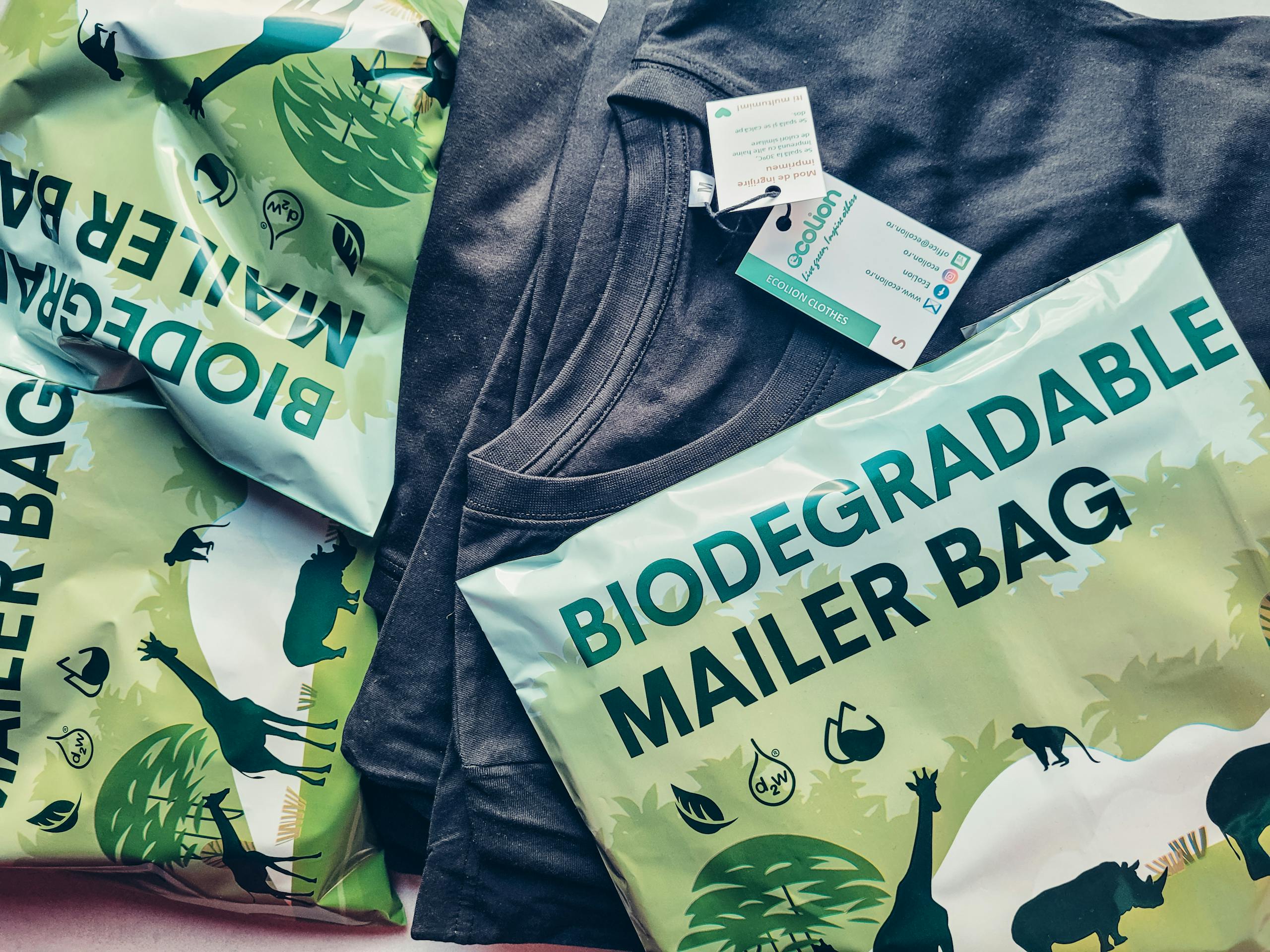 Close-up of biodegradable mailer bags and sustainable shirt promoting eco-friendly packaging.