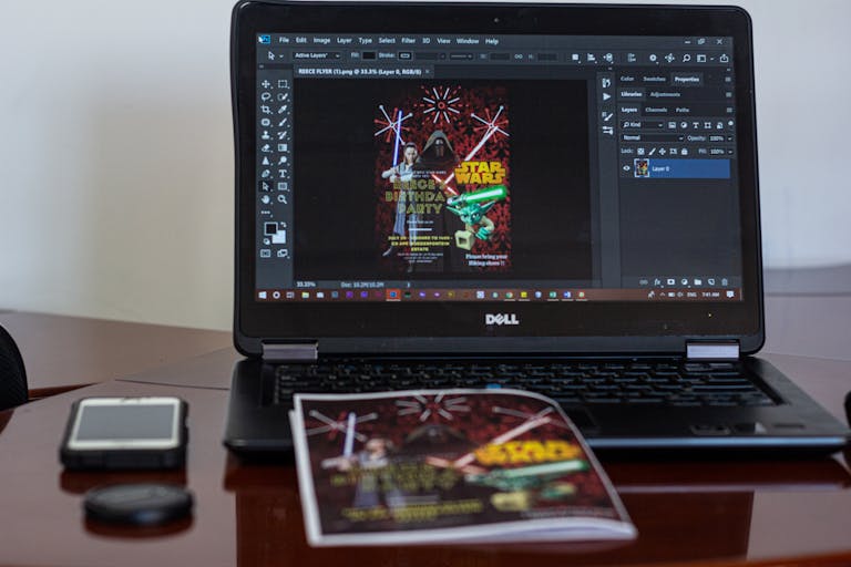 A laptop displaying Star Wars party invitation design in a workspace setting.