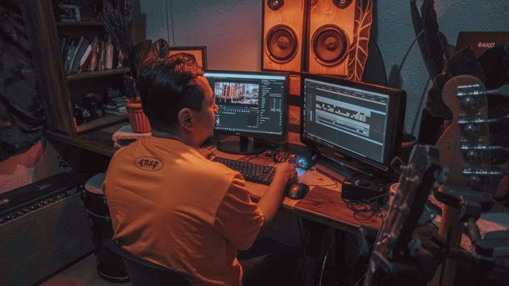 A person is editing video footage on dual monitors in a home studio with music equipment.