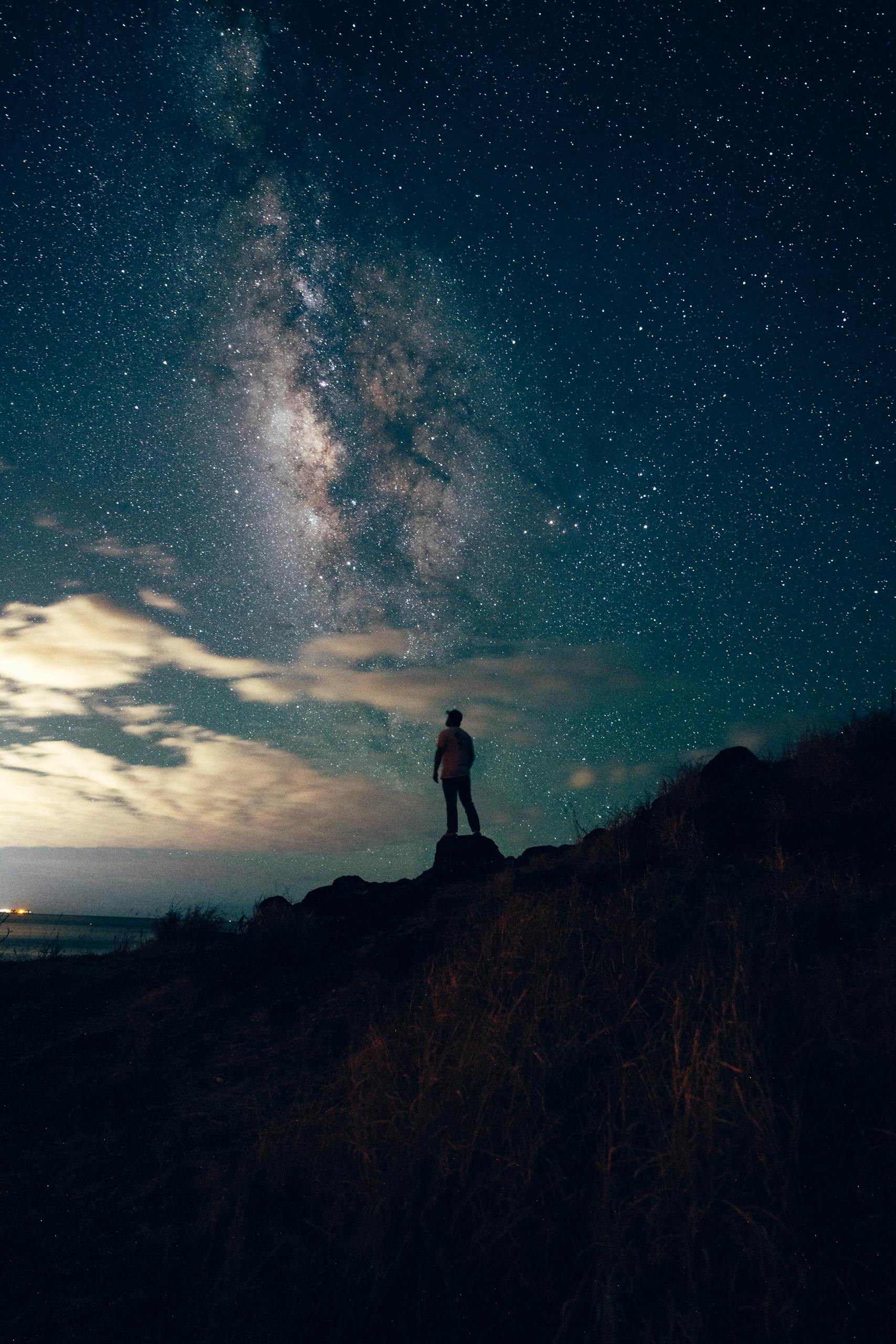 Silhouette of a person under a starry night sky and Milky Way.